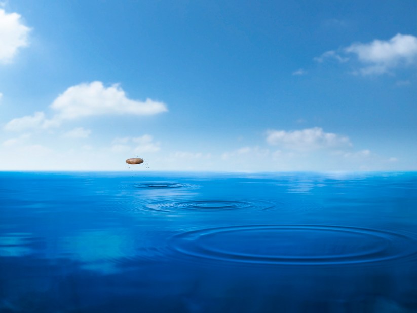 a stone skipping across blue water under a nearly cloudless sky