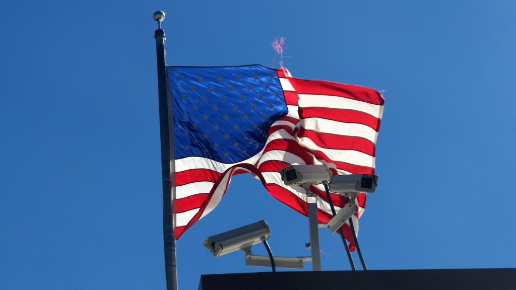 Low Angle View Of Flag surrounded by security cameras Waving Against Clear Blue Sky