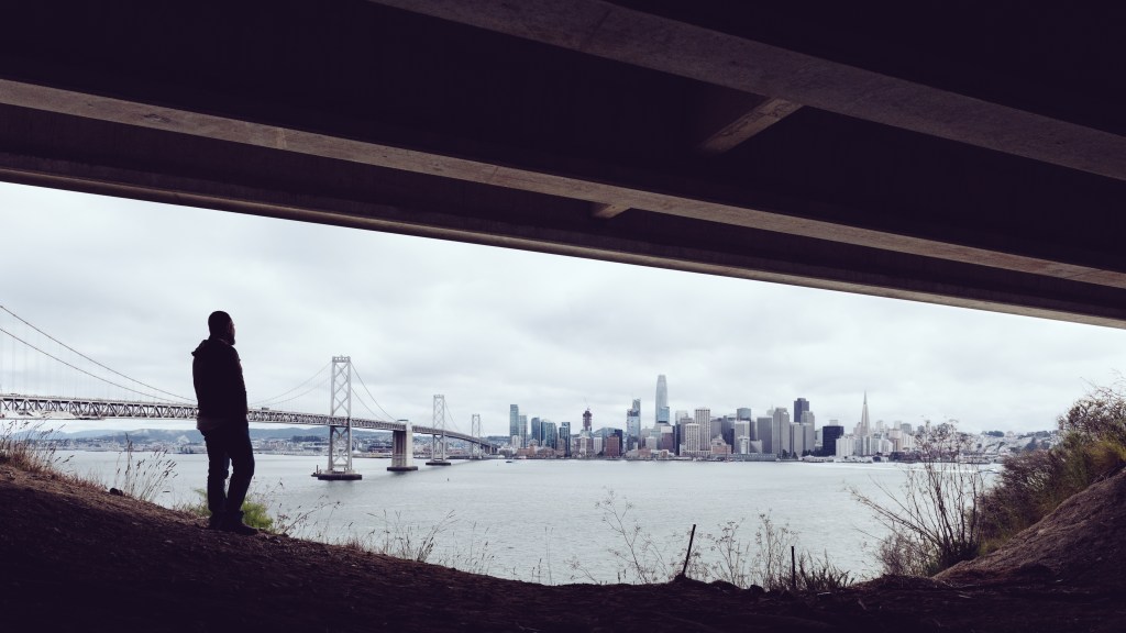 Image of a man under a bridge with the San Francisco skyline in the background.
