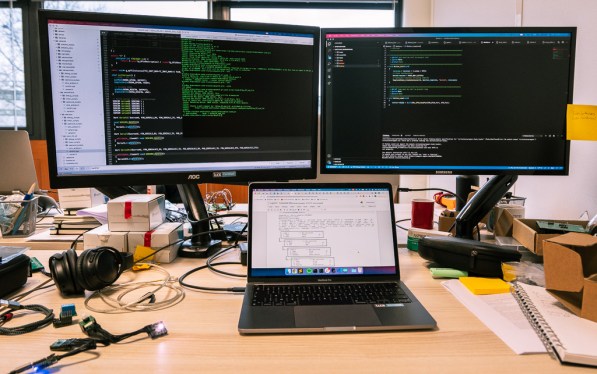 Luos on laptop with two large external monitors behind it.