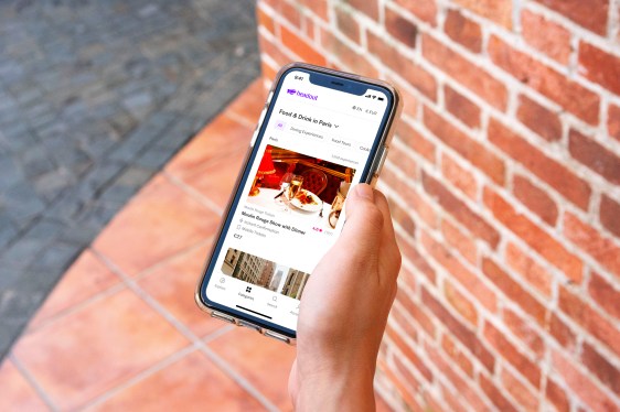 A closeup of a hand holding a smartphone opened to Headout's travel activity booking app