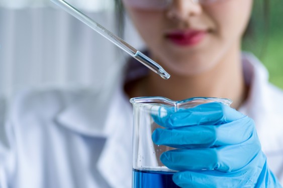 Lab worker dropping sample into beaker of blue liquid