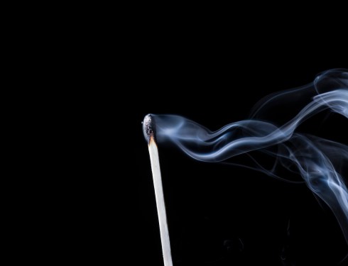 A recently extinguished wooden match with smoke drifting out of frame.