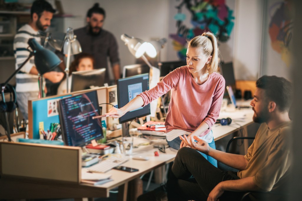 Group of computer programmers working in the office. Focus is on blond woman showing something to her colleague on PC.