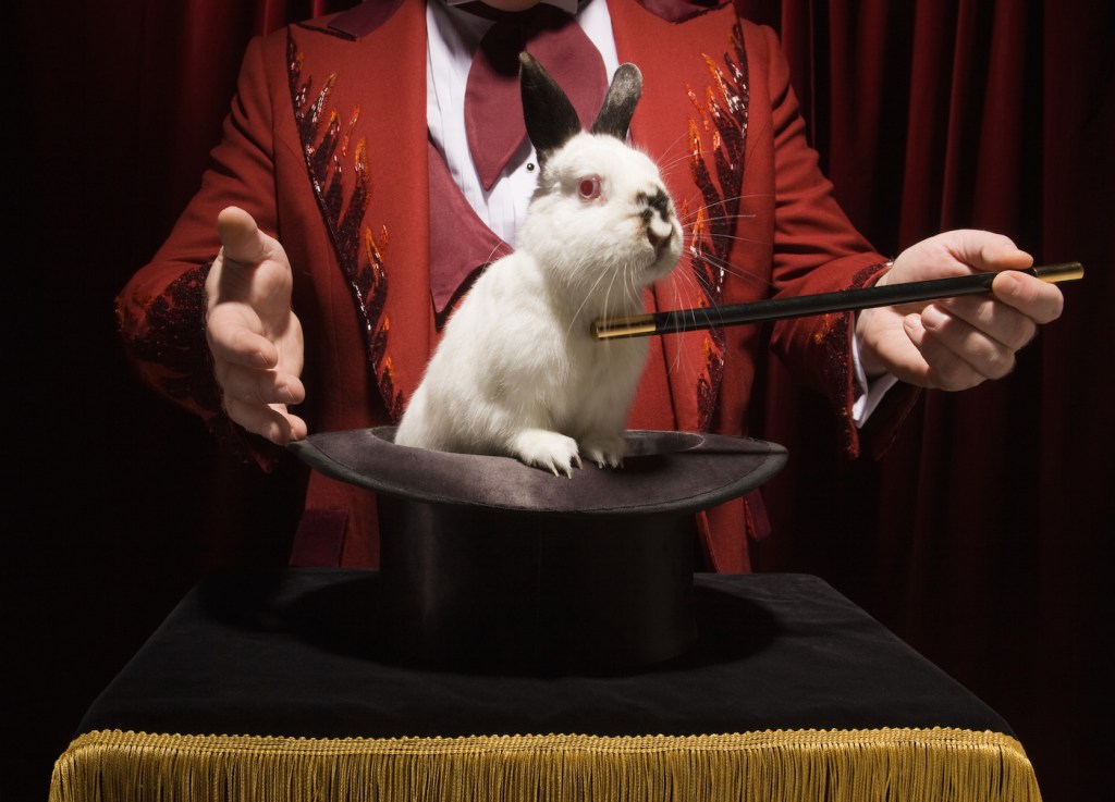 Magician taking rabbit out out of a magic hat with wand.