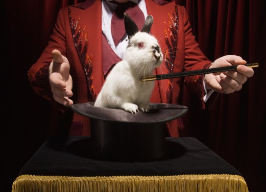 Magician taking rabbit out out of a magic hat with wand.