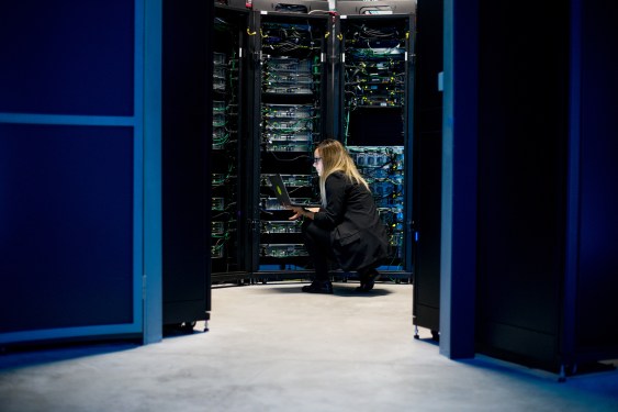 Female IT Professional Working in Server Room With Laptop.