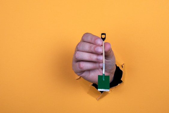 Miniature shovel in a woman's hand. Work and diligence concept. Orange background