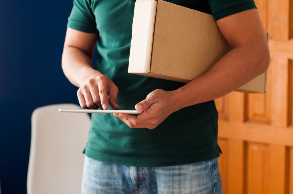 Midsection of a young adult Southeast Asian man holding a carton box package and digital tablet indoors, used in a story about Philippines-based buy now, pay later startup Plentina