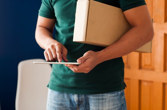 Midsection of a young adult Southeast Asian man holding a carton box package and digital tablet indoors, used in a story about Philippines-based buy now, pay later startup Plentina