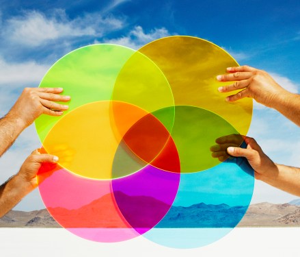 Hands holding multi-colored discs in landscape.