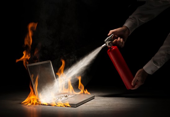 Businessman using fire extinguisher on laptop computer that is in flames