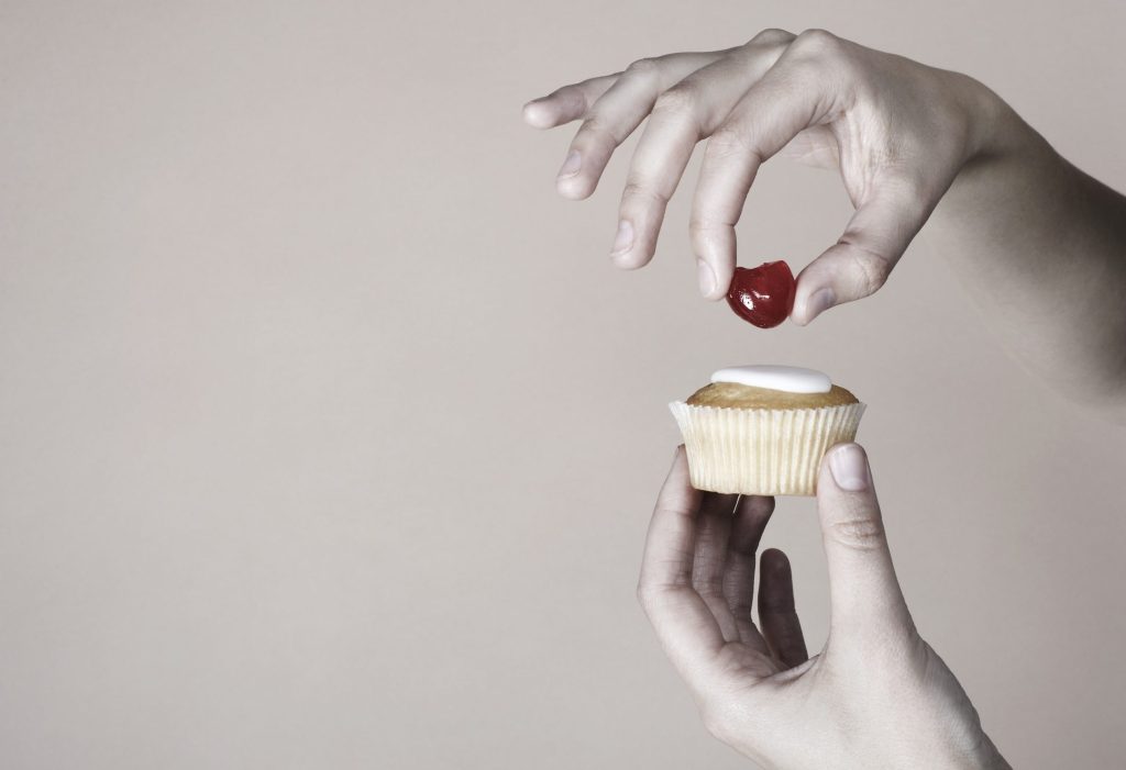 Hand placing cherry on top of cup cake