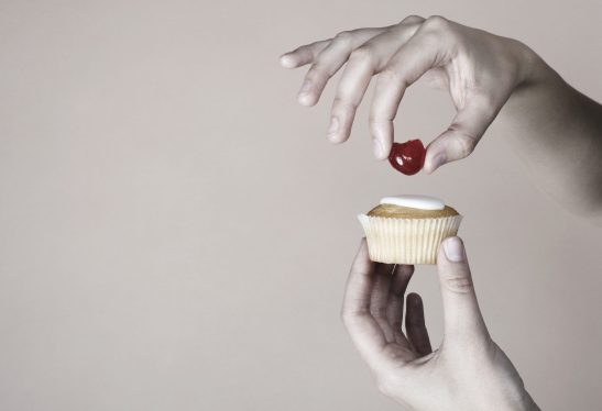 Hand placing cherry on top of cup cake