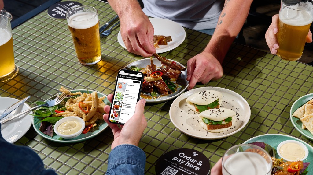 Mr Yum's mobile ordering system, with a person holding a phone over a QR code at a restaurant