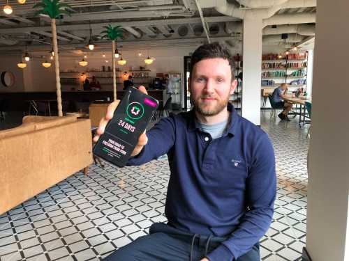 Remojo's founder Jack Jenkins holding up a smartphone showing the app