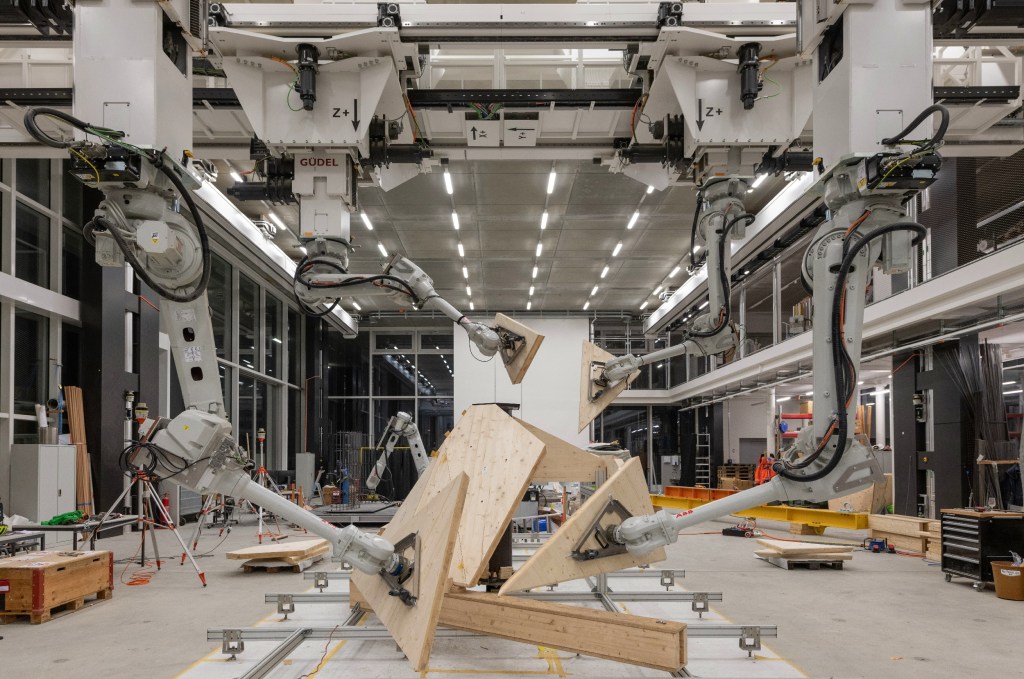 Robot arms hold various sections of the Semiramis structure in a workshop.