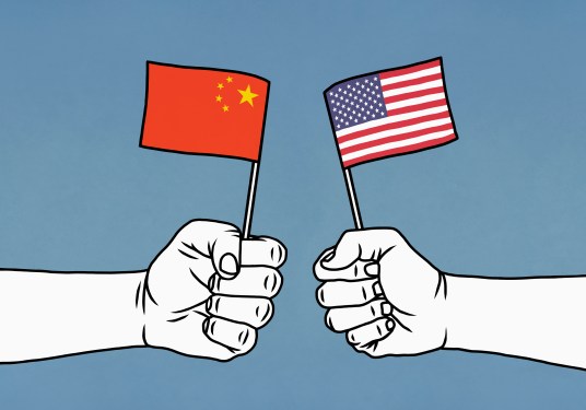 Hands clenching Chinese and American flags on blue background