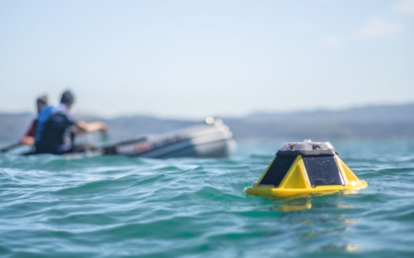 A Sofar buoy sensor floats in the ocean by a boat.