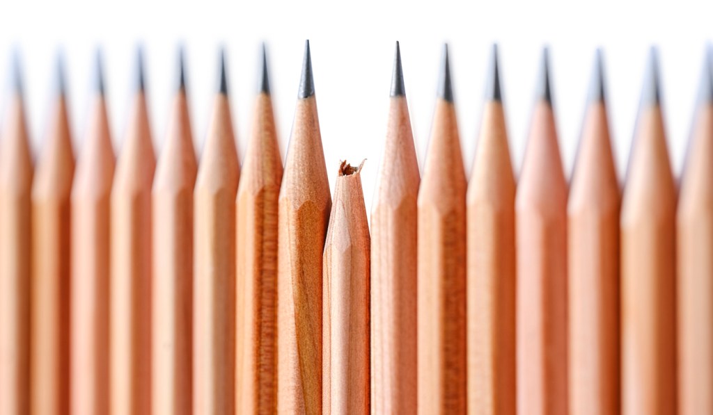 Row of very sharp wood pencils on a white background with one broken pencil sitting slightly lower down among them. Concept image relating to standing out from the crowd, broken, inferior, different, under achievement etc. Shallow depth of field, focus on the blunt pencil. isolated on white, clipping path included.