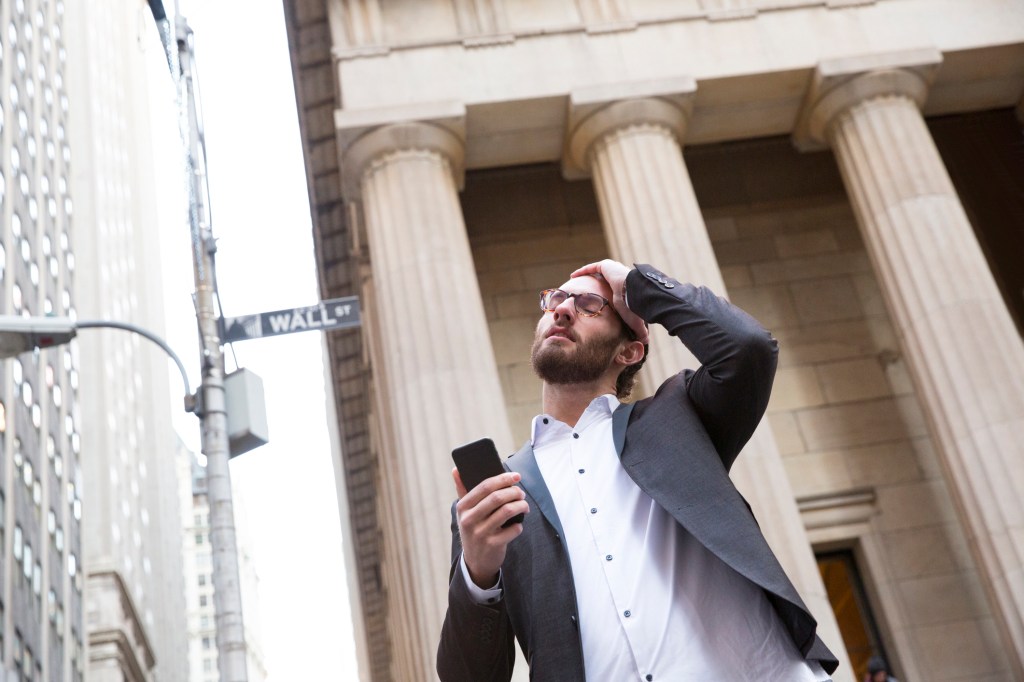 Portrait of worried young businessman with cell phone in front of Stock Exchange, New York City, USA