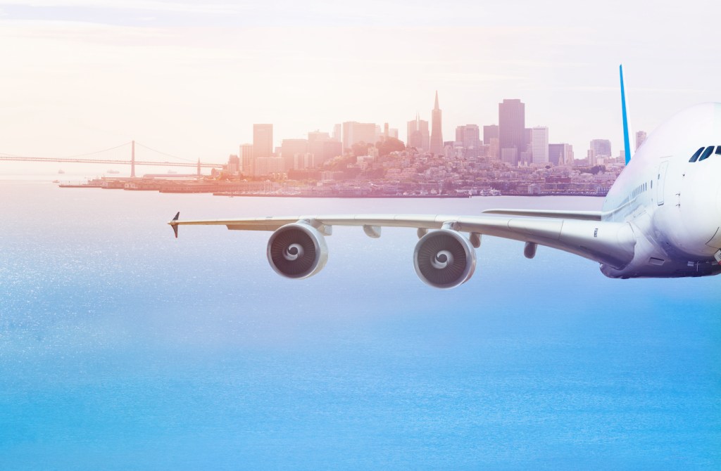 Front view of airplane mid air over San Francisco Bay that is flying away from the city.