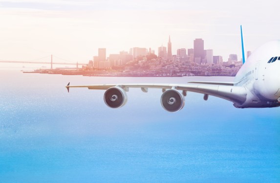 Front view of airplane mid air over San Francisco Bay that is flying away from the city.