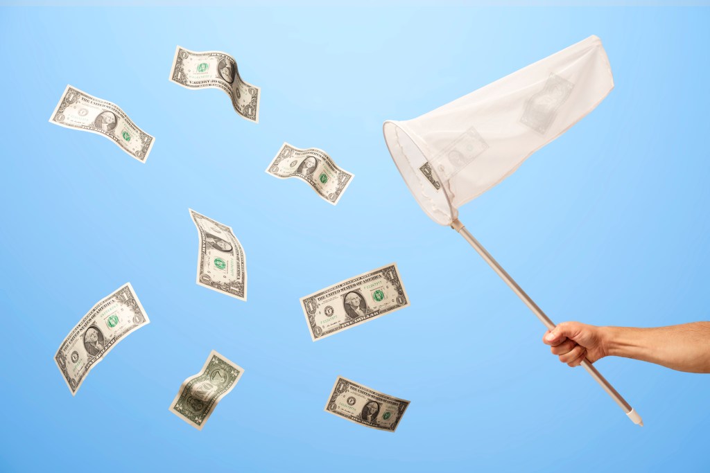 Man's hand with butterfly net catching US 1 dollar bills that are floating in mid air on blue background