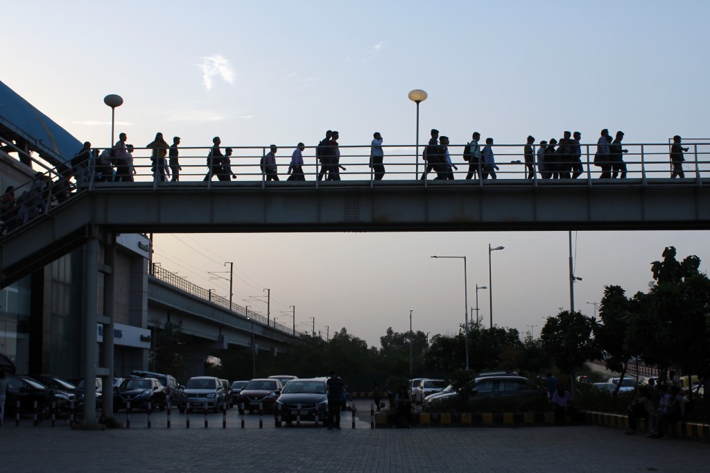 Daily commuters of Delhi Metro are seen coming out of Metro station, on a raised walkway