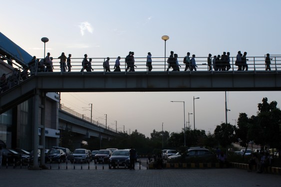Daily commuters of Delhi Metro are seen coming out of Metro station, on a raised walkway