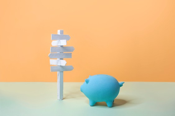 One big piggy bank and an empty road sign on coloured background.