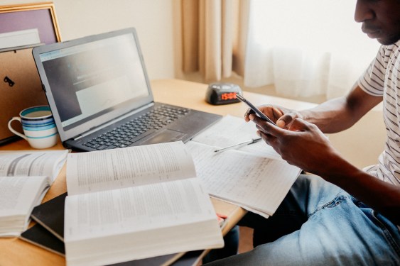 Cropped shot of a focused young man texting on his cellphone while trying to study inside of his apartment room during the day, used in an article about Singapore-based edtech Cialfo