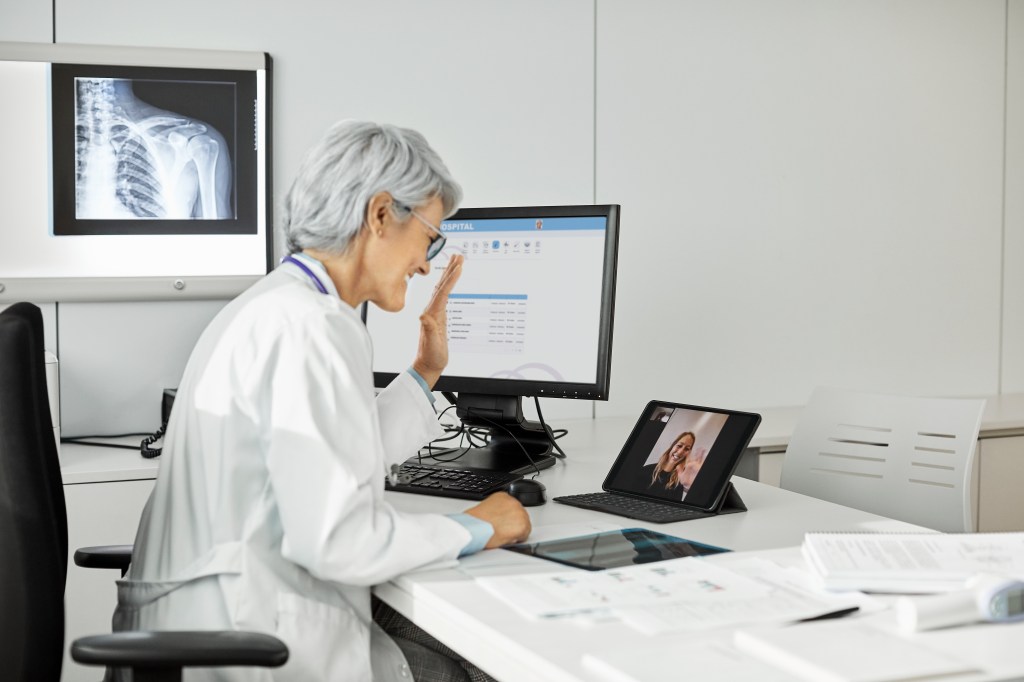 Image of a doctor waving her hand at a tablet during a telemedicine visit.