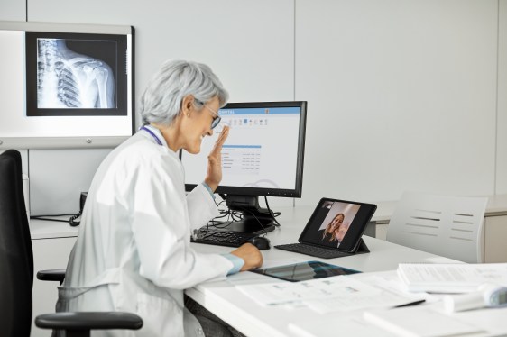 Image of a doctor waving her hand at a tablet during a telemedicine visit.