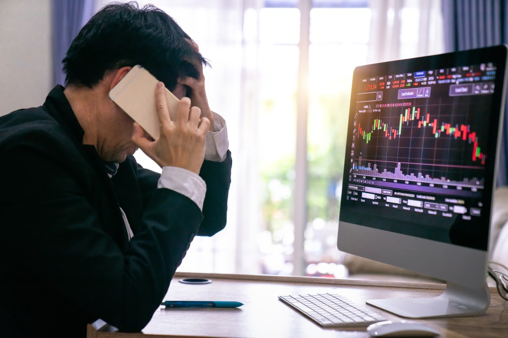 Image of a stressed businessman looking at screen of falling stocks.