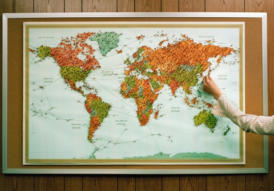 Image of a woman's hand sticking pins on a global map.