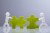 Side View Of Two Miniature Human Figures Solving Green Jigsaw Puzzles On Grey Background