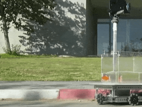 A fish in a tank with wheels moves along a street.