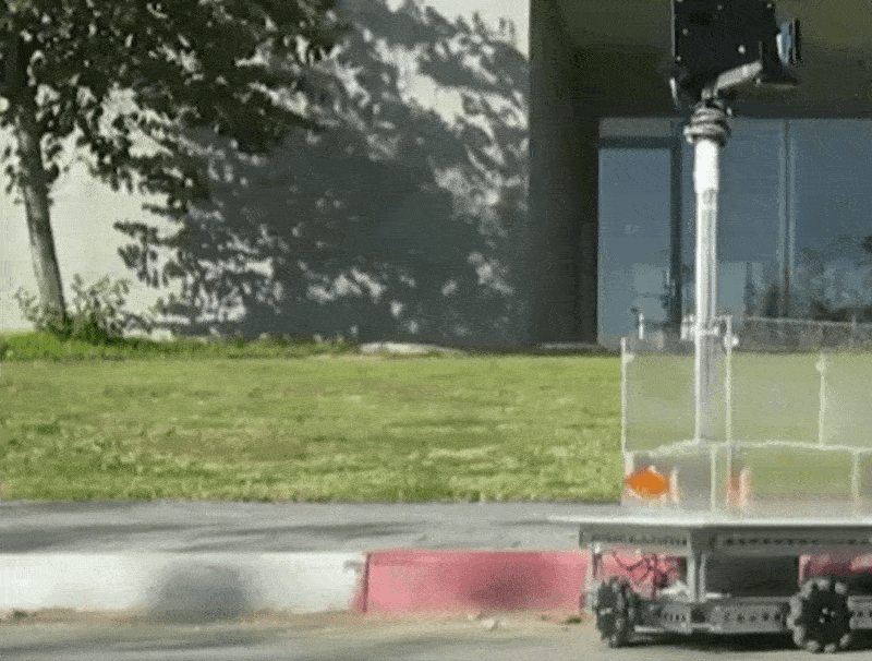 A fish in a tank with wheels moves along a street.
