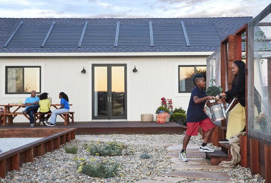 A family plays in front of a home with solar shingles installed.