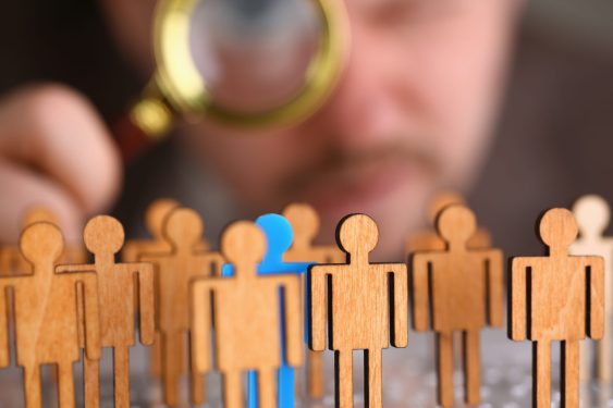 Image of a man looking through a magnifying glass at small statuettes to represent the hiring process.