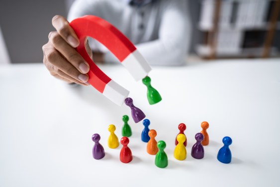 Person using a magnet to attract pawns on a table representing customers