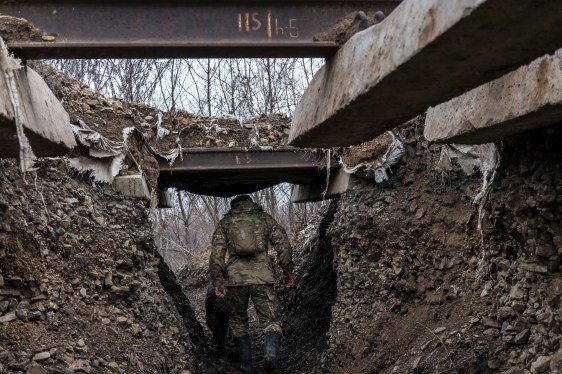A Ukrainian soldier walks through a trench away from the camera