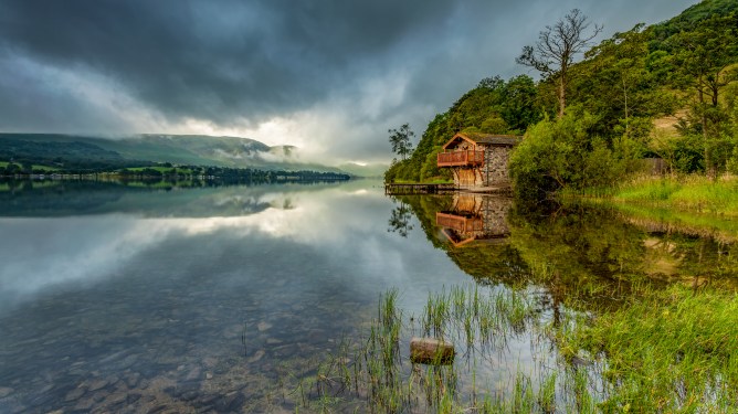 The Duke of Portland Boathouse reflecting in the waters at Ullswater. Storm clouds gather in the sky above.