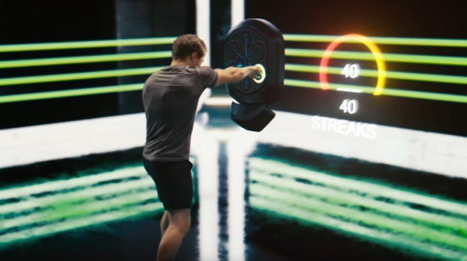 A Liteboxer athlete punches a black device amid a green, techno-looking room