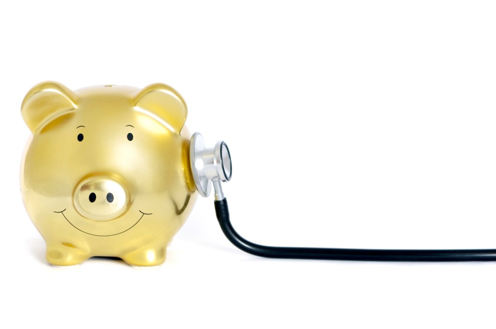 Conceptual image of a gold piggy bank and stethoscope isolated on pure white, selective focus on the piggy bank