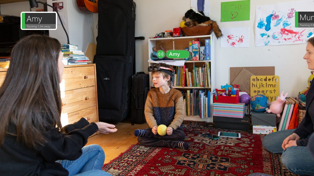 A young blind boy sits in a group wearing the PeopleLens prototype.