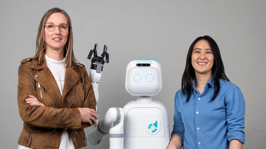 Diligent Robotics co-founders, Dr. Andrea Thomaz and Dr. Vivian Chu pose with Moxi, a robot they created to help take the stress off of nurses and clinical care teams.