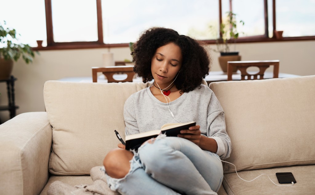 Shot of a young woman writing in a notebook on the sofa at home