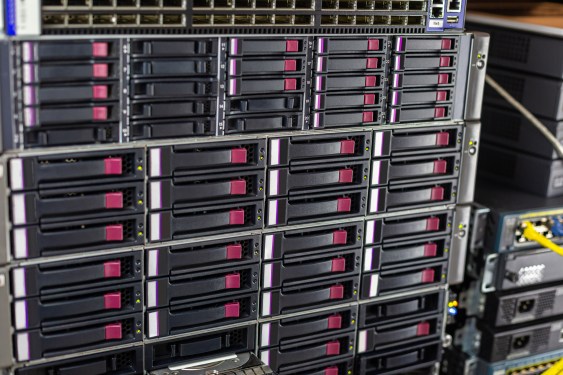 Array of hard drives in a computer data center server rack with plugs for LAN cables above in a close up detailed full frame view in a cloud computing concept